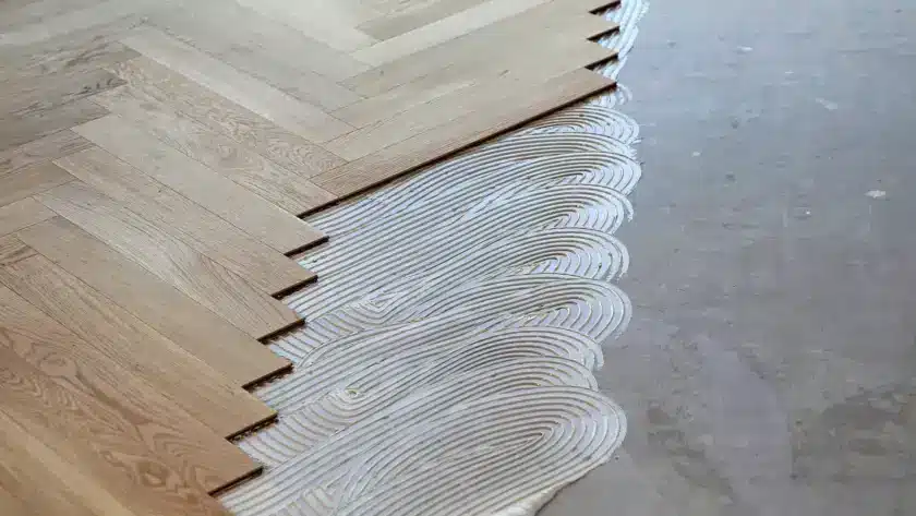 Herringbone parquet installation over concrete subfloor with precise plank placement.