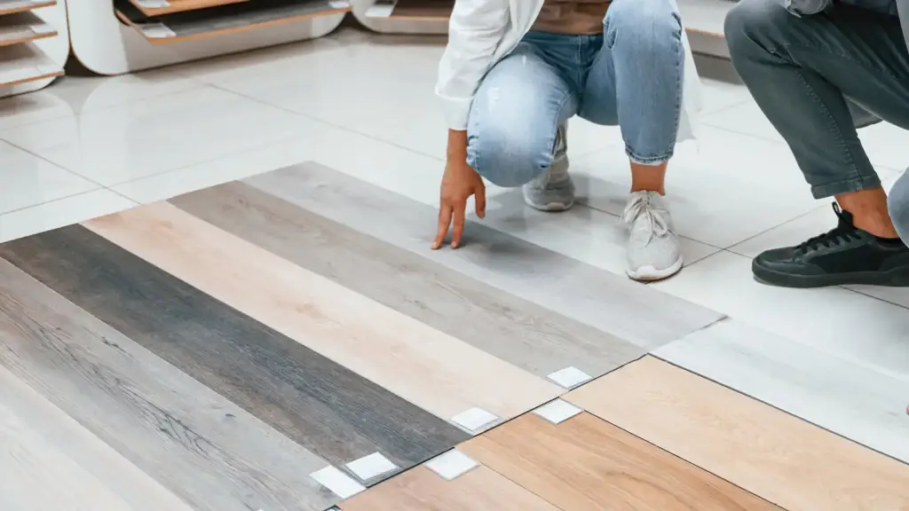 Homeowner comparing rigid core vinyl plank samples laid over white ceramic tile