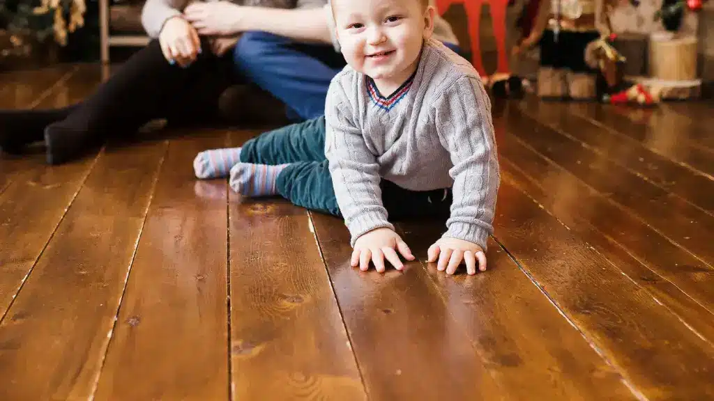 Toddler crawling on a wide plank hardwood floor showing seasonal gaps between boards